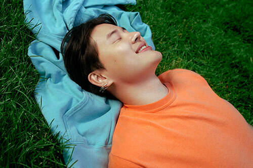 Man laying in the grass, using a hoodie as pillow, and wearing Comfort Colors C1717 Heavyweight Ring Spun Tee in “melon”.