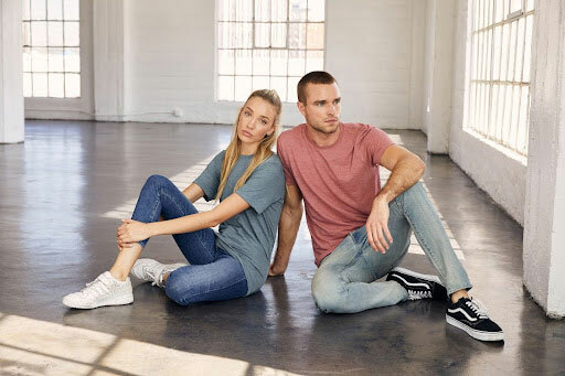Man and woman sitting on the floor wearing the Bella+Canvas’ 3650 in Denim and 3650 in Mauve Slub.