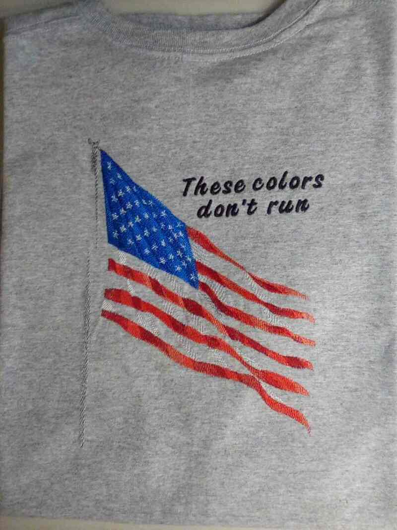 Grey heathered t-shirt with embroidered American flag design and the words these colors don’t fun