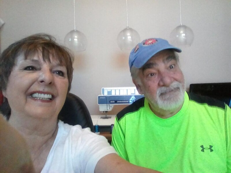 Married couple, Paul and Mary Magnus, taking a selfie in their workspace with their embroidery machine