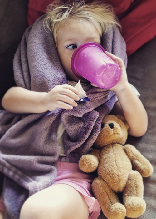toddler laying next to teddy bear with sippy cup